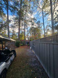 A golf cart parked next to a gray fence in a backyard with tall trees.