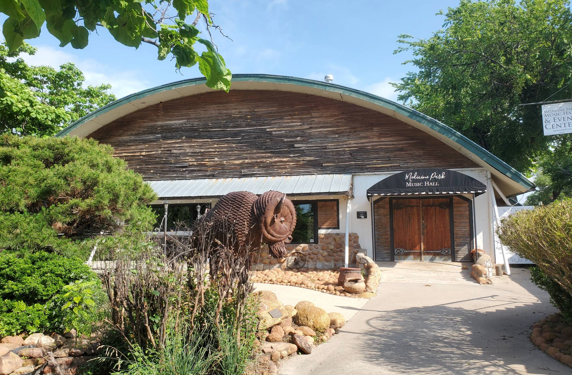 Rustic building with a curved roof, wooden entrance, and stone path in a sunny garden setting