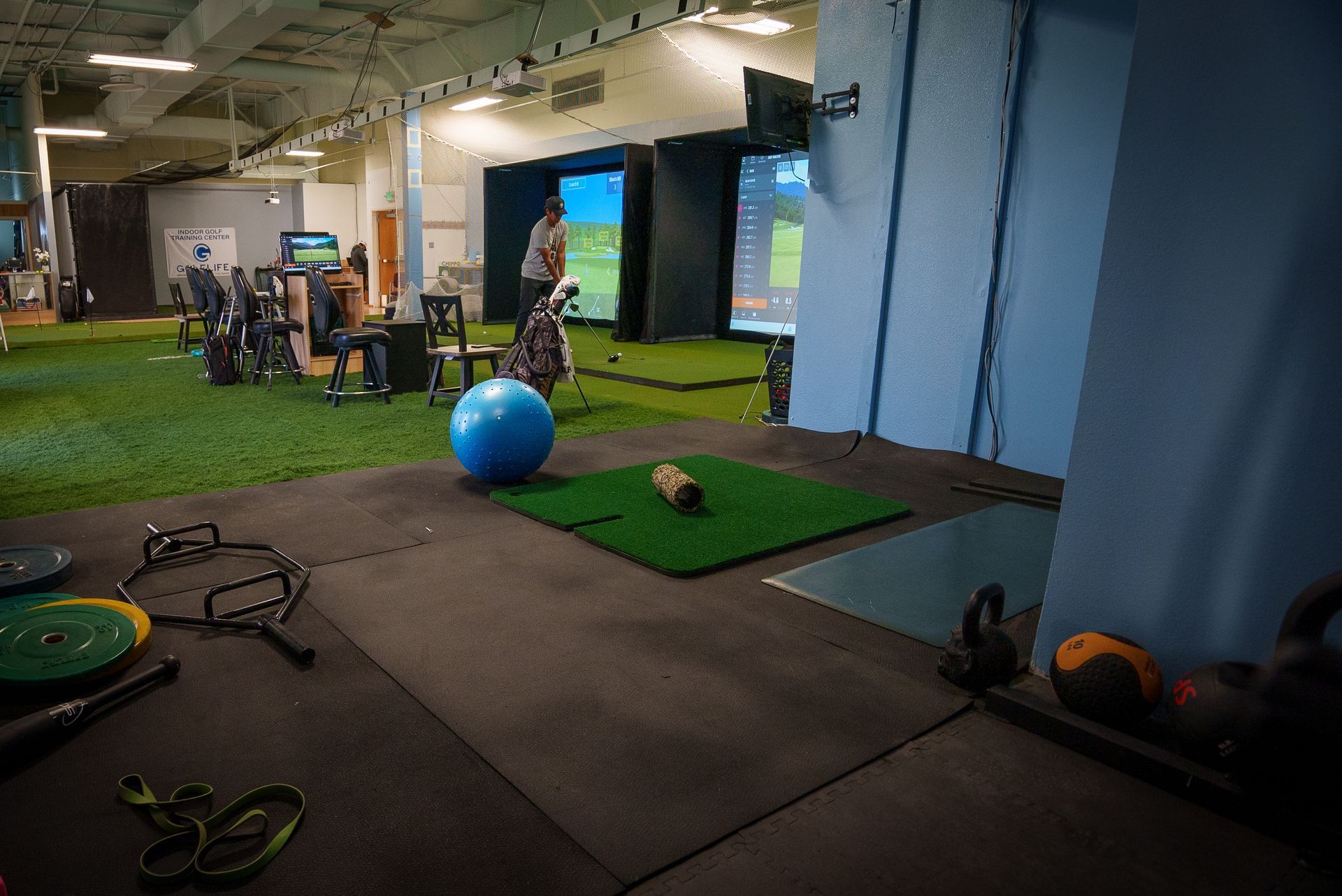 Indoor golf and fitness area. People playing golf on simulators, exercise equipment visible.