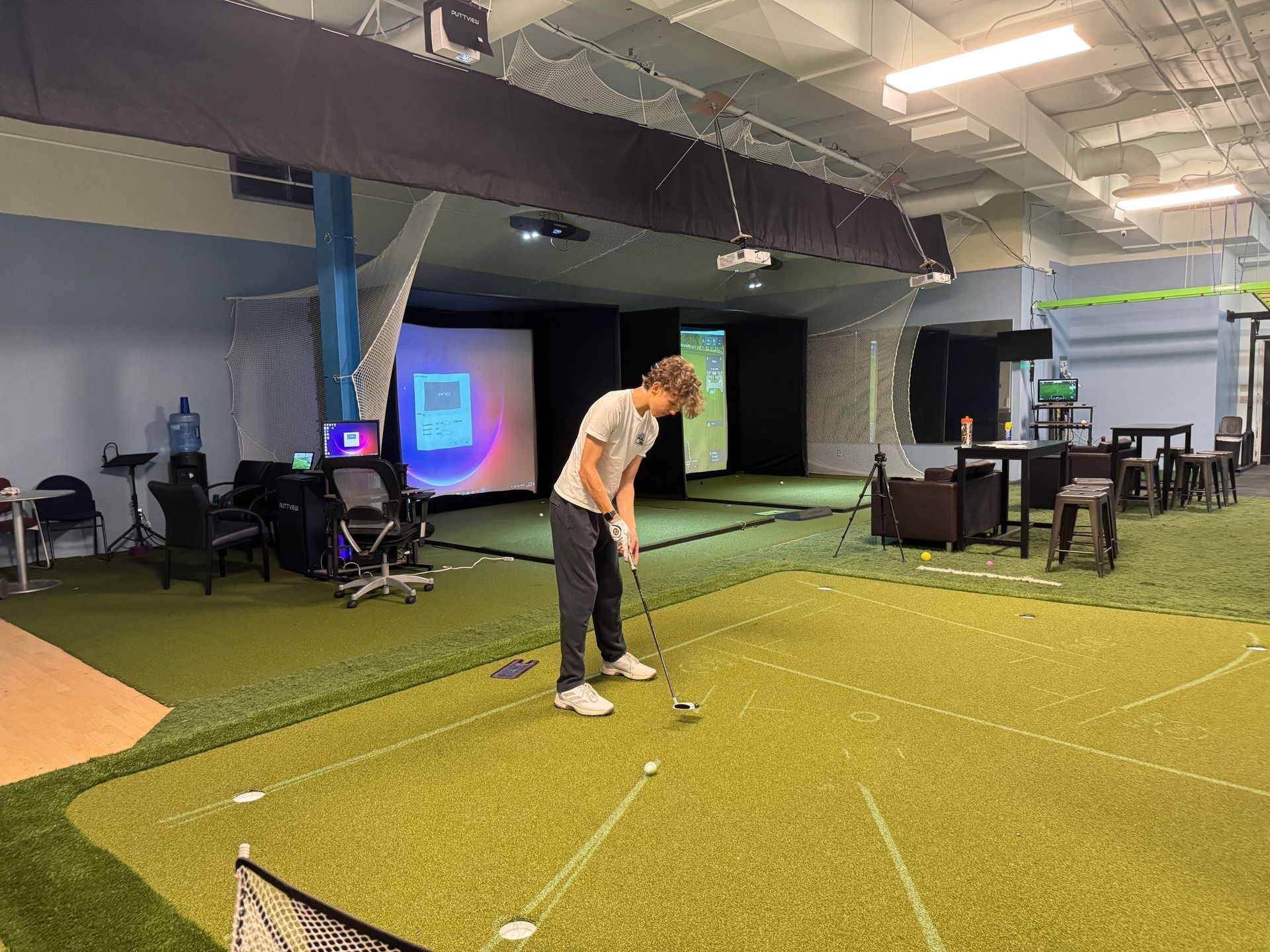 Person putting on an PuttView indoor putting  green with target lines and screens in the background