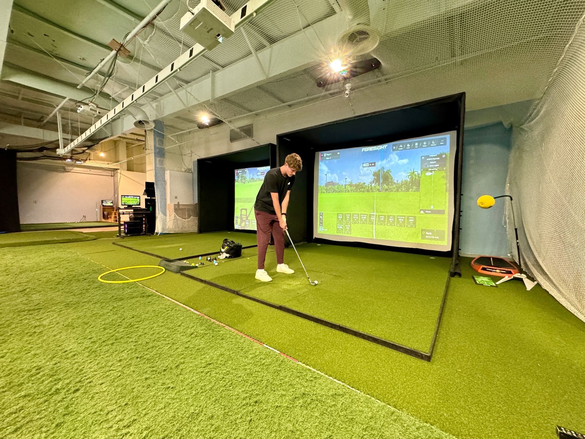 Golfer putting in an indoor simulator bay with a large screen and green turf