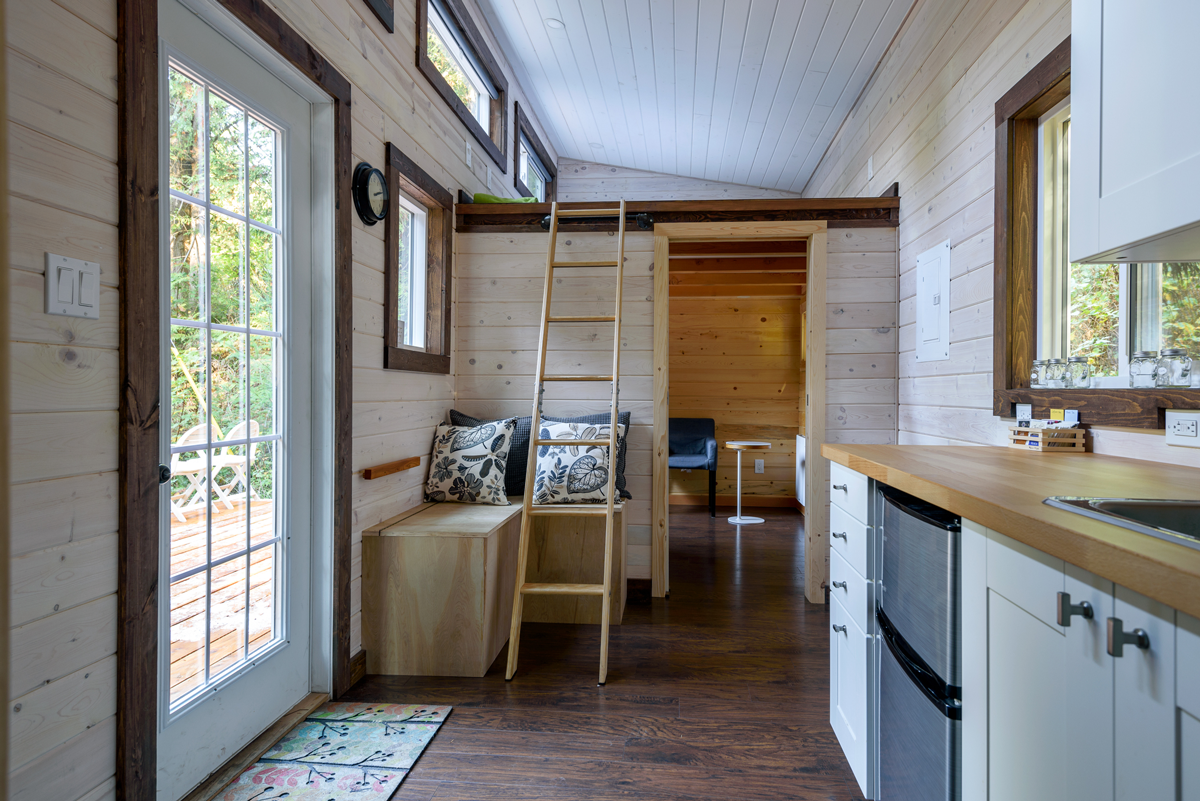 Interior of a tiny home with a ladder, wood walls, and a view of a deck through a glass door.