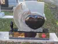 A white marble headstone with a black heart carving. A vase sits at the base.