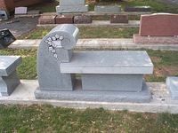 Gray granite bench with an artistic curved back, displayed outdoors.