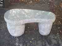 Stone garden bench with curved seat, supported by two cylindrical legs.