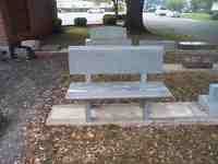 Gray bench on a concrete pad in front of a building, surrounded by leaves and other paving stones.