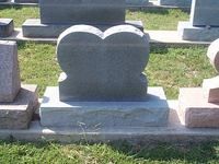 Gray double heart-shaped headstone on a rectangular base, set in a grassy cemetery.