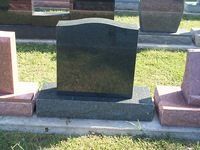 Black granite headstone with curved top, sitting on a rectangular base in a grassy setting.