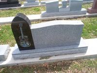 Gray granite headstone with black guitar inlay, outdoors.