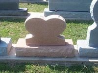Heart-shaped pink granite headstone on a rectangular base in a grassy cemetery.