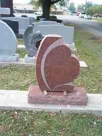 Red heart-shaped tombstone with white accents, on a rectangular base, in a cemetery.