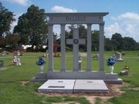 Grave site with gray pillars, a cross, and the name 