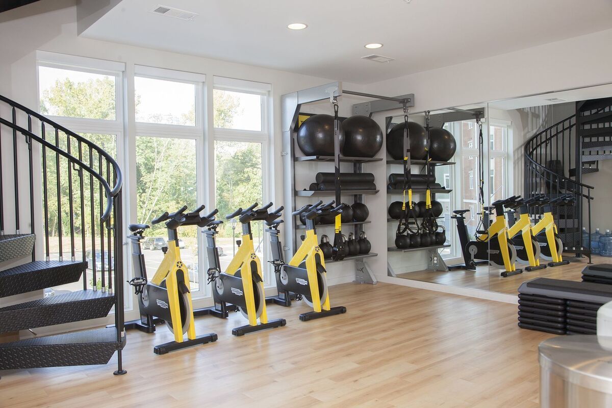 A gym with a spiral staircase , exercise bikes , and a large mirror.
