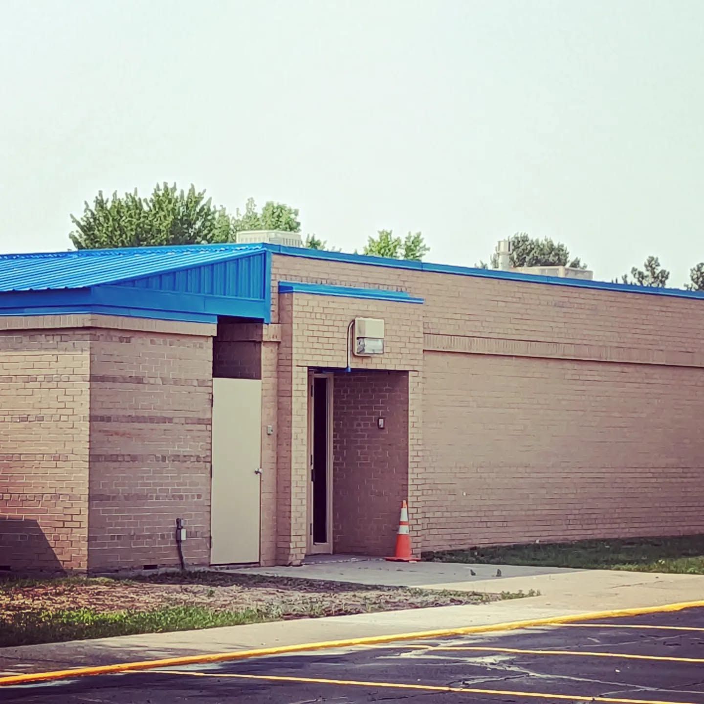 Small beige building with a blue roof and doorway beside a road