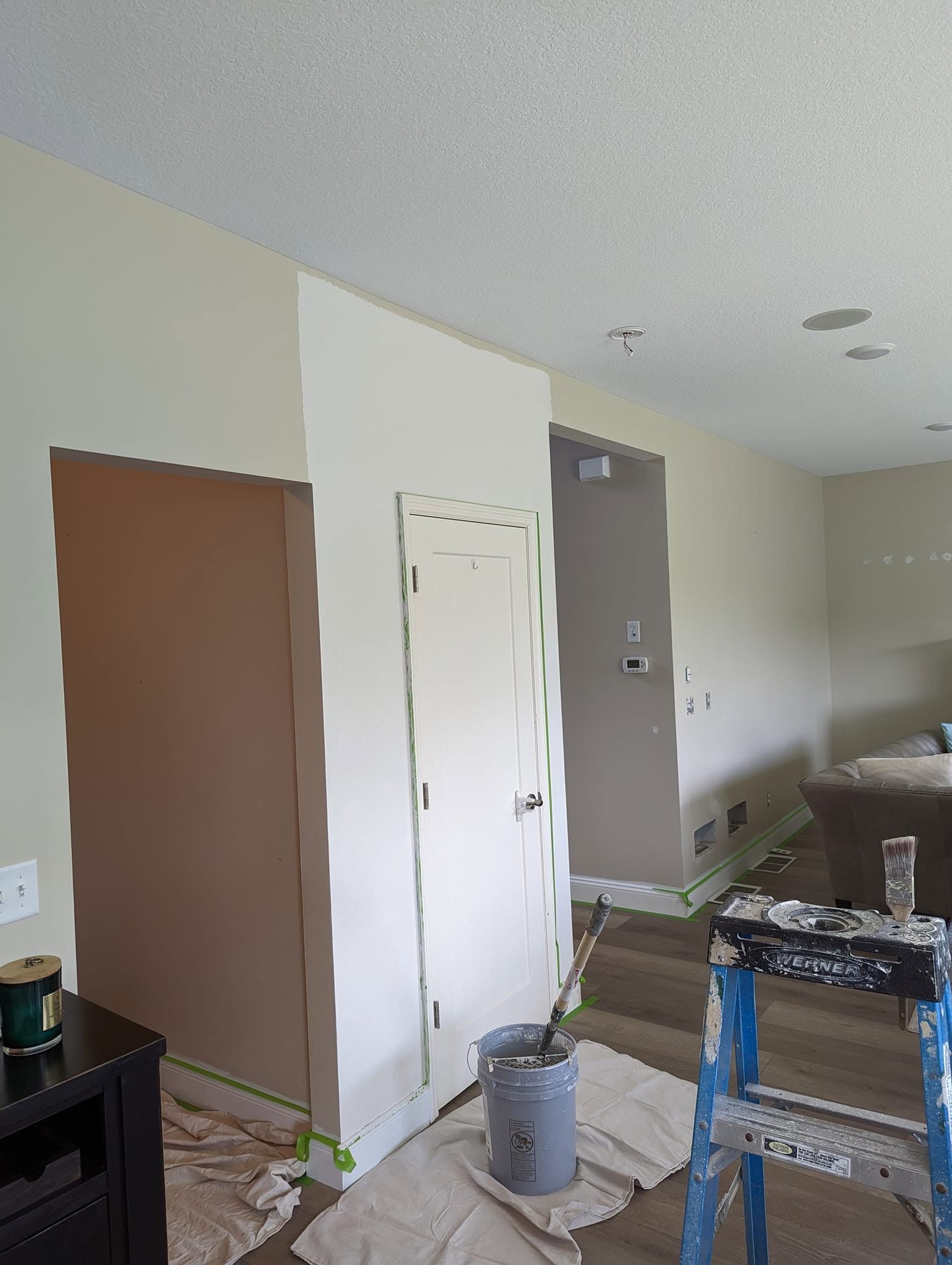 Partially renovated room with brown and white doors, paint supplies, and a ladder near a stairway