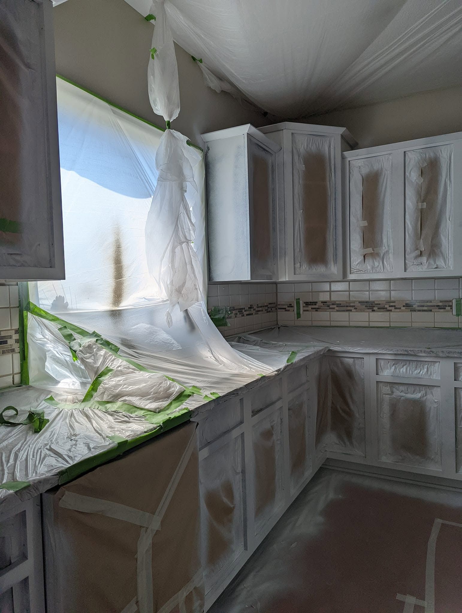 Damaged kitchen with white cabinets, broken drywall, and a collapsed ceiling by the window