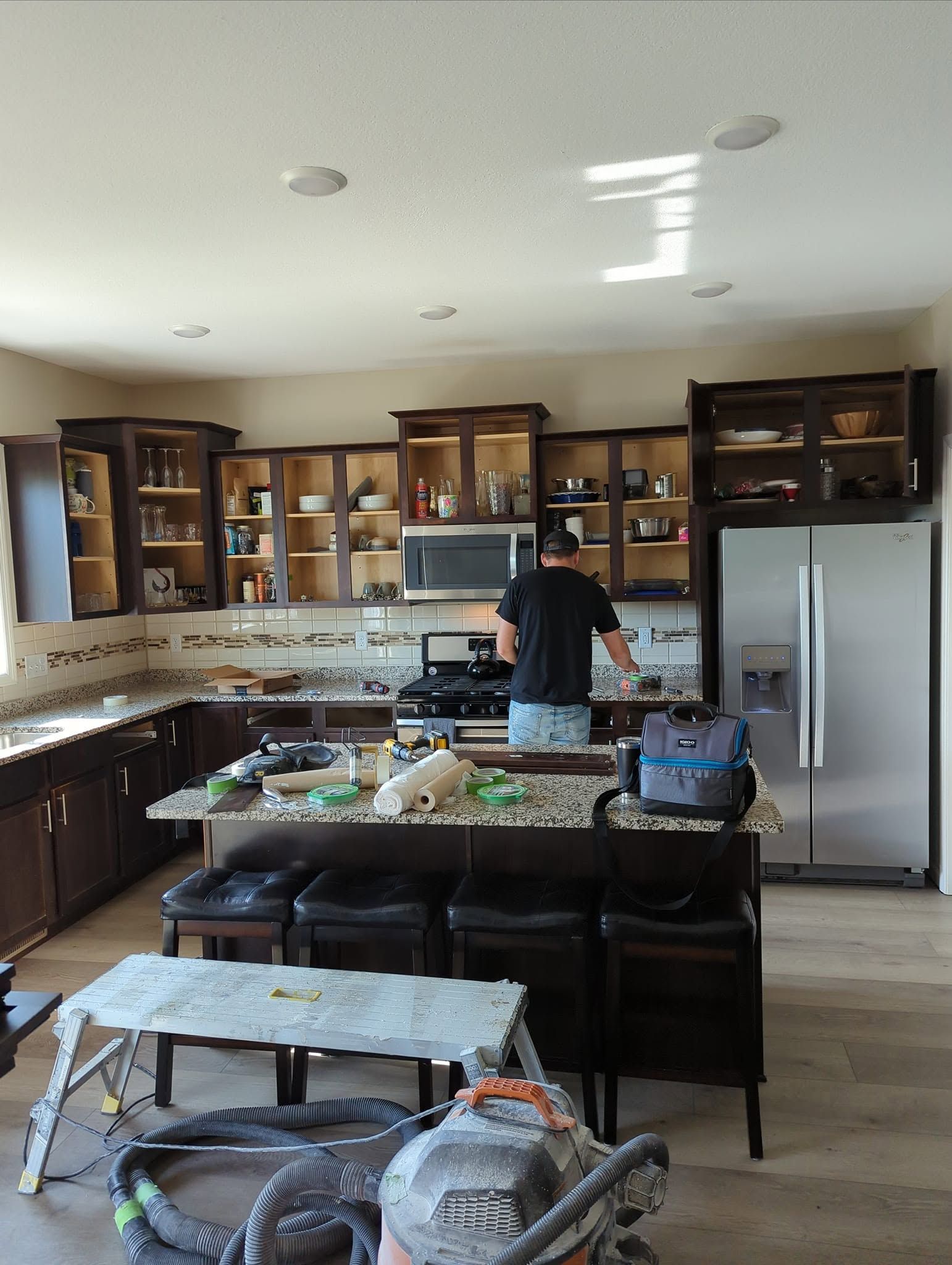 Modern kitchen with dark wood cabinets, a stainless fridge, and a person standing at the island preparing food.