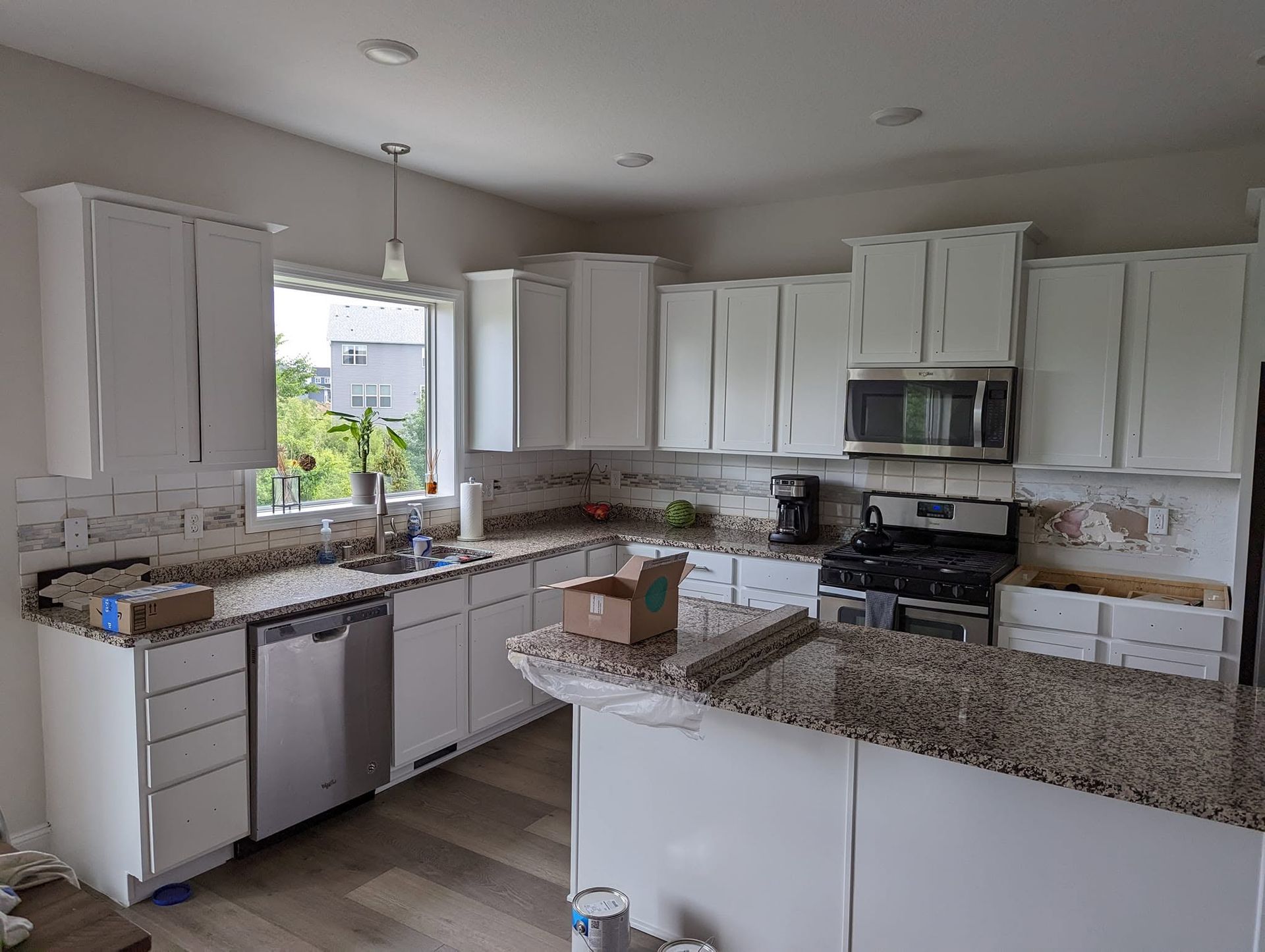 Bright white kitchen with granite counters, white cabinets, stainless appliances, and a window above the sink