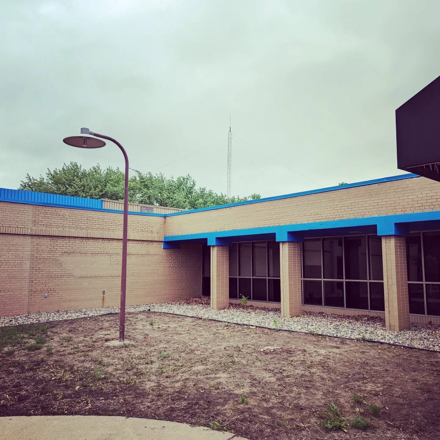 Empty courtyard with a lamp post, tan brick walls, blue roof trim, and a cloudy sky