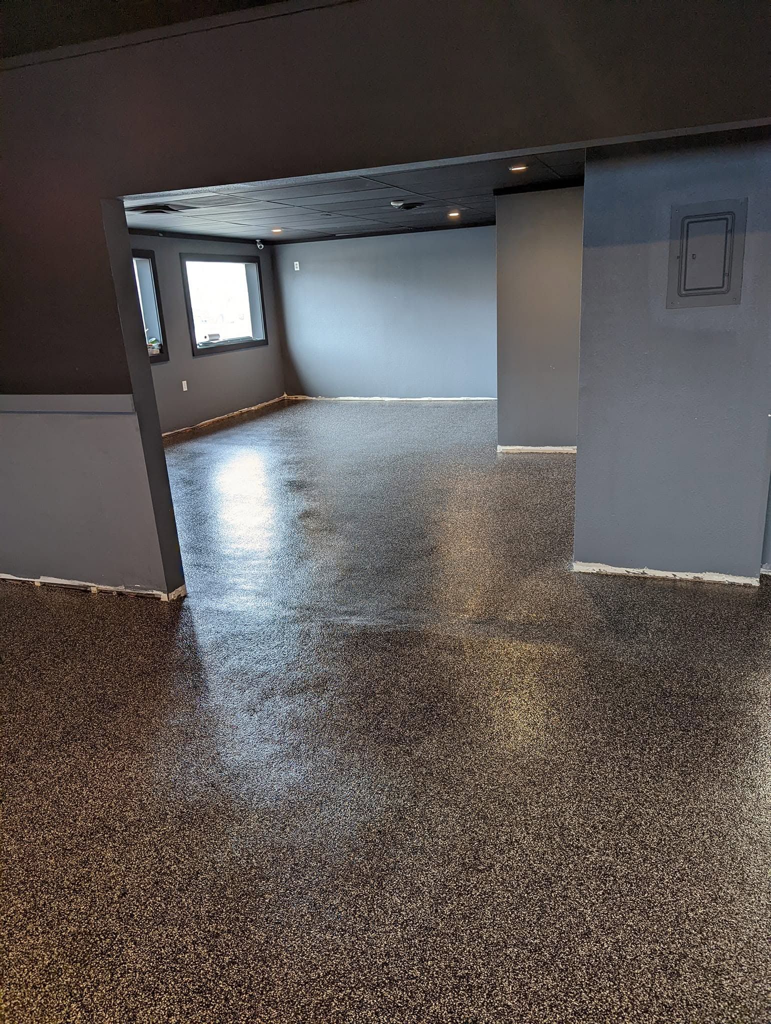 Empty room with speckled floor, gray walls, a window, and an open doorway to a brighter space