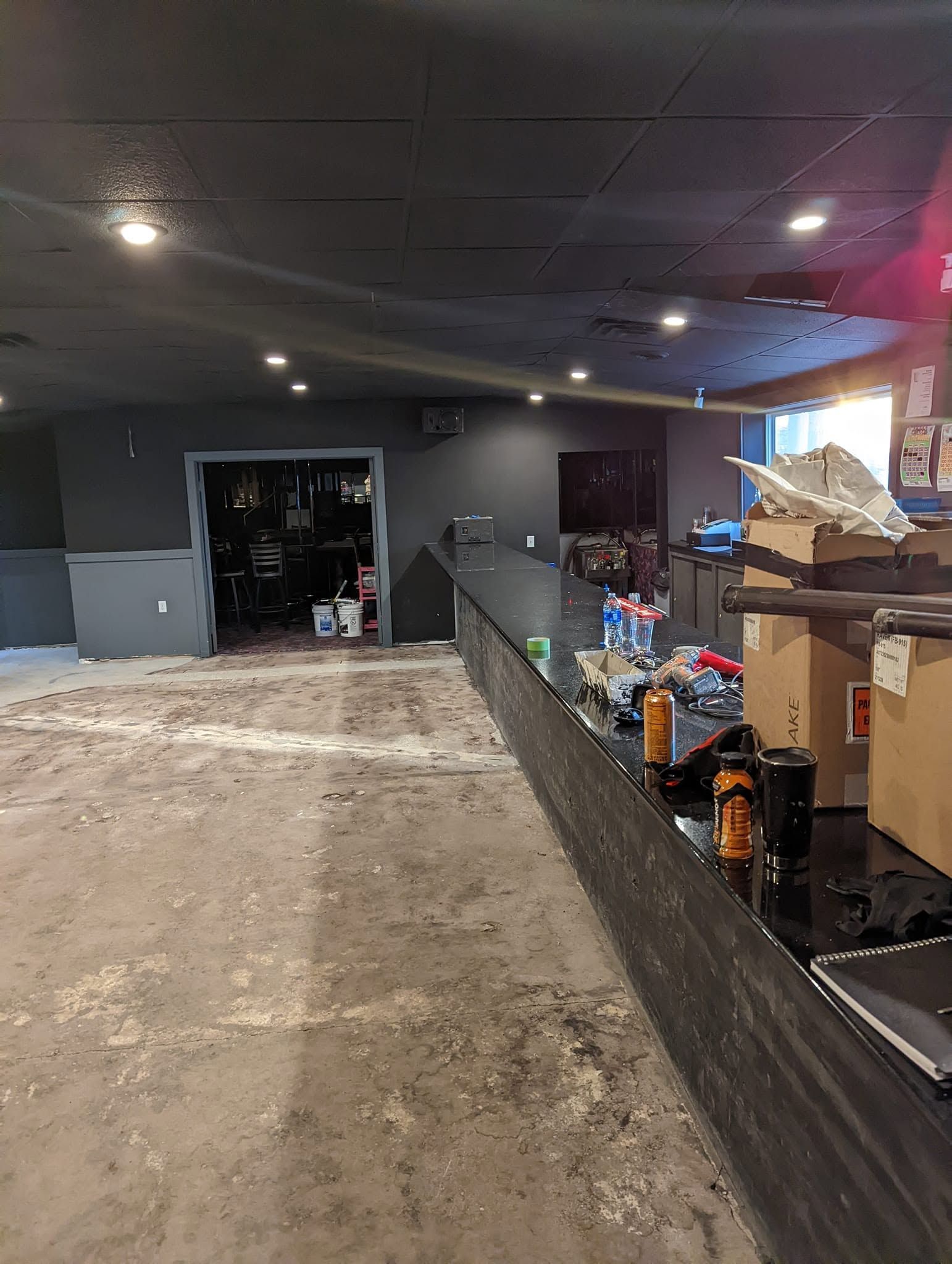 Partially cleared room with debris-covered floor, shelves of supplies, and a dark open doorway.