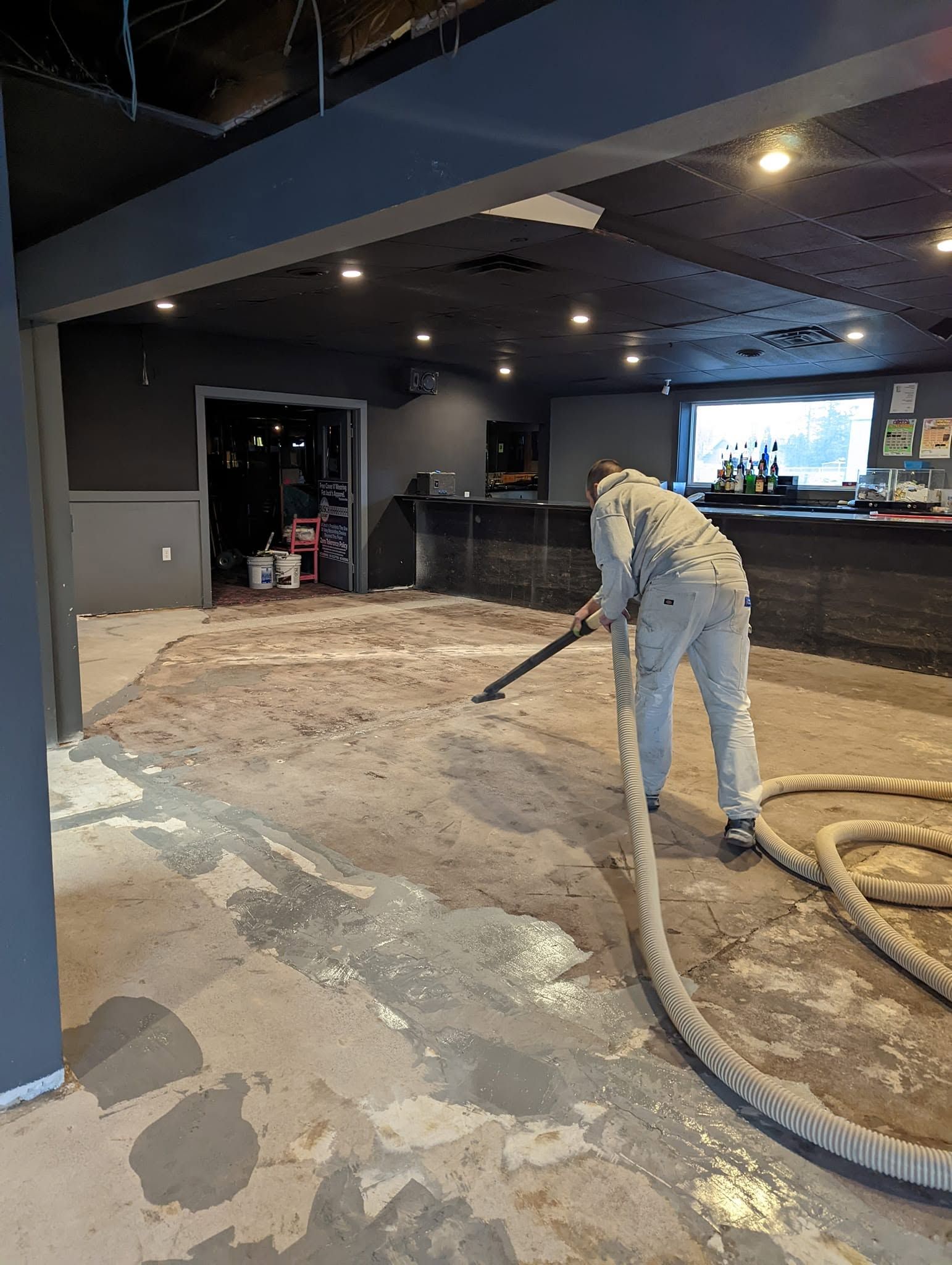 Worker smoothing concrete floor inside a dim commercial space with hoses and equipment nearby