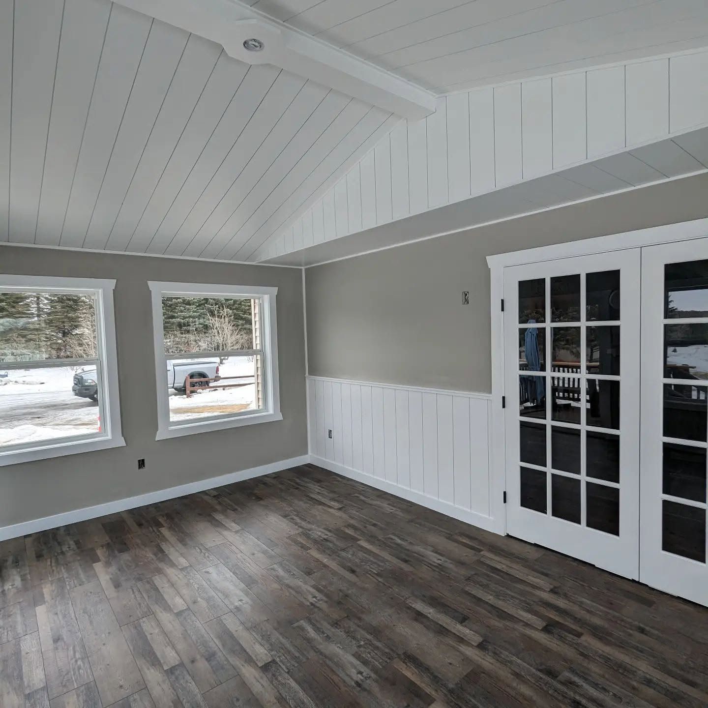 Bright empty room with vaulted white ceiling, gray walls, dark wood floor, and French doors to the outside