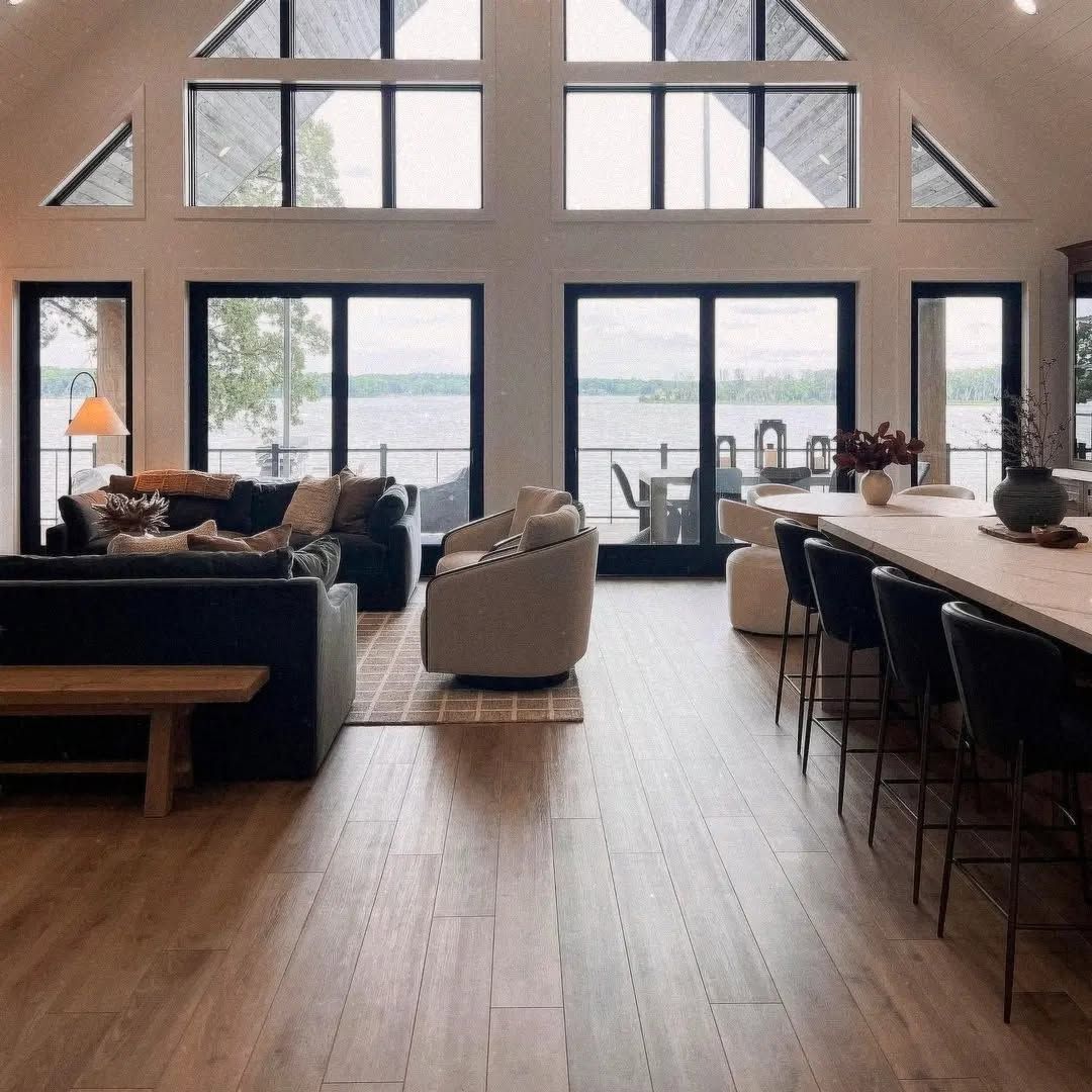 Modern open-plan living room with tall windows, wood floors, sofa, chair, dining table, and mountains outside
