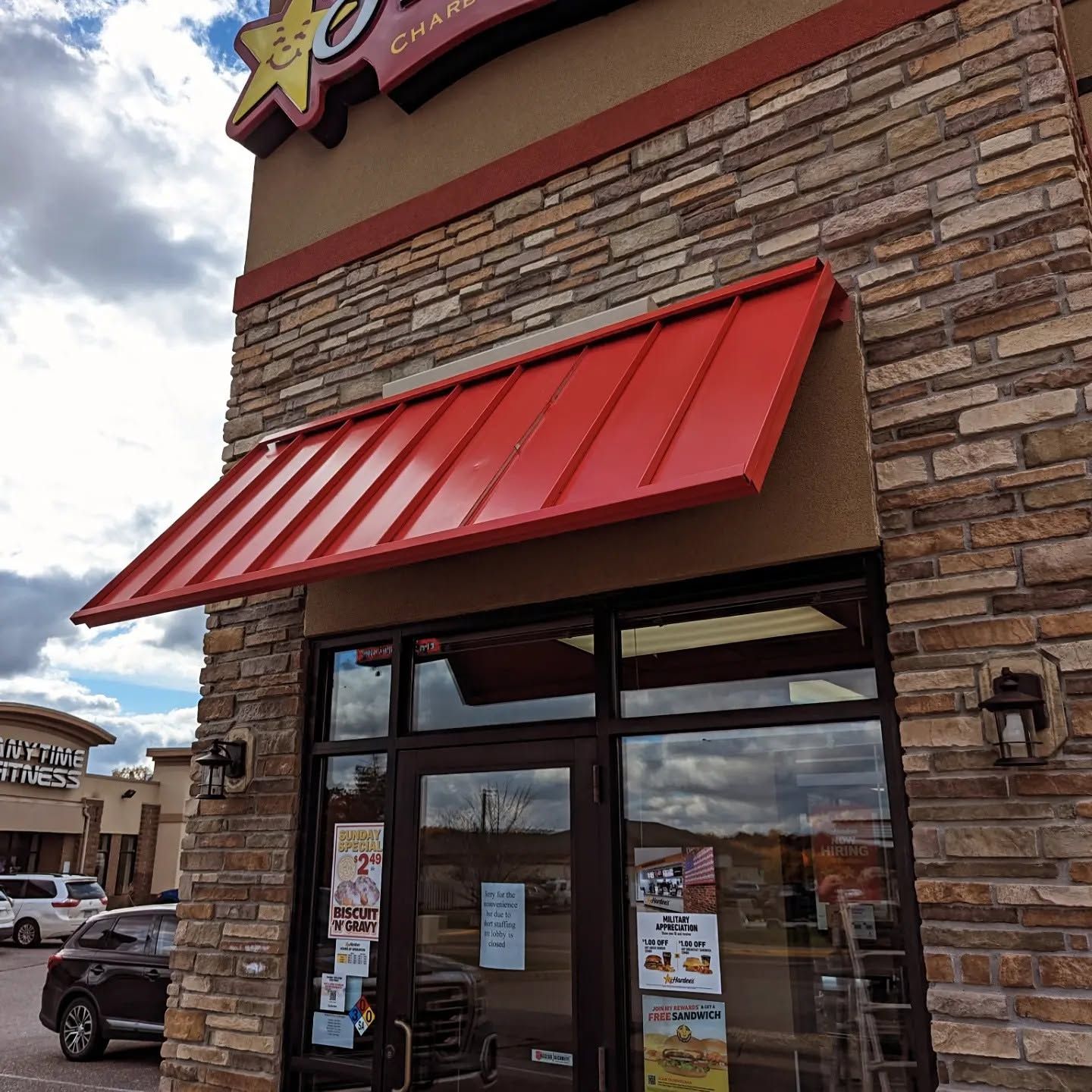 Storefront with a red awning and stone facade under a cloudy sky