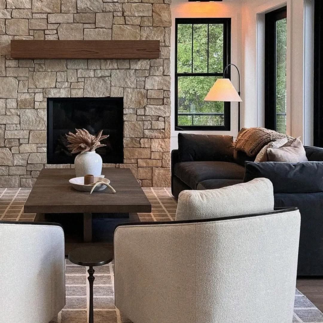 Modern living room with stone fireplace, dark sofa, wooden table, and large windows