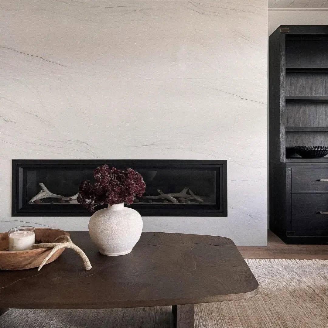 Minimalist room with a dark table, white vase of dried flowers, and a black fireplace mantel