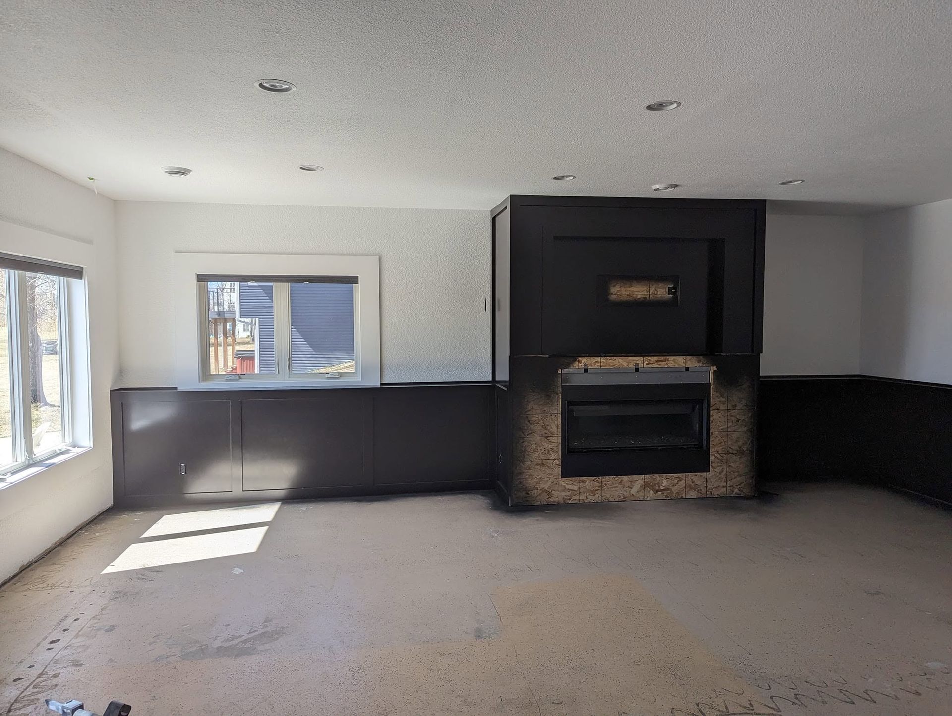 Empty living room with large windows, gray carpet, and a brick fireplace on the far wall.