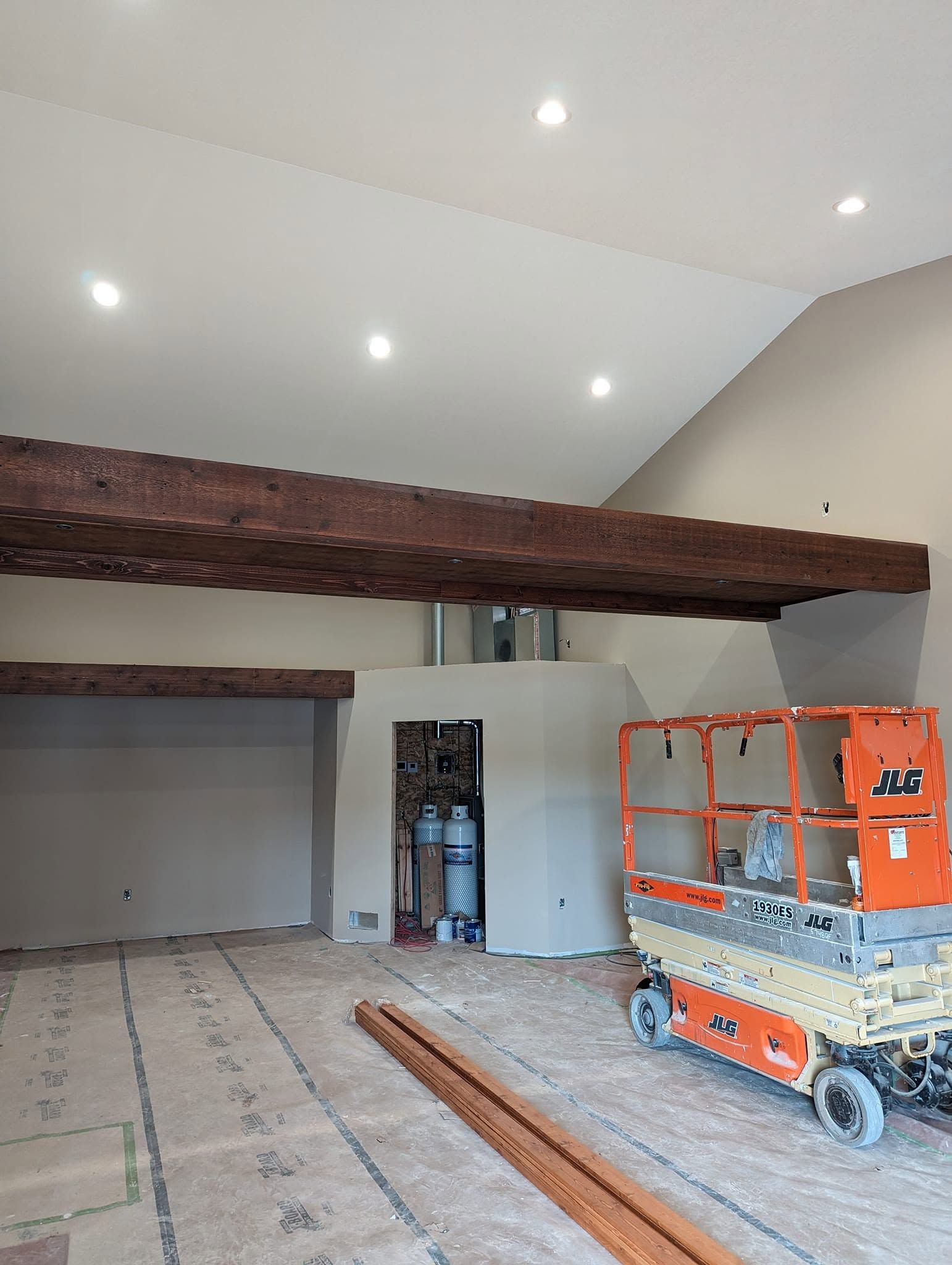 Large unfinished room with exposed wood beam, recessed lights, and an orange scissor lift inside