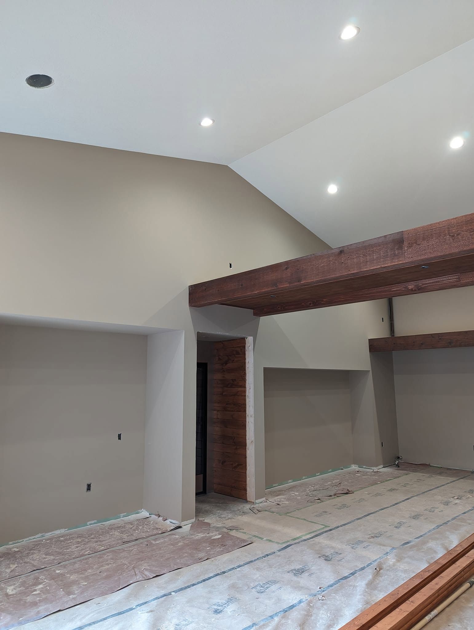 Empty room under construction with vaulted ceiling, exposed brick beams, and protective floor covering.