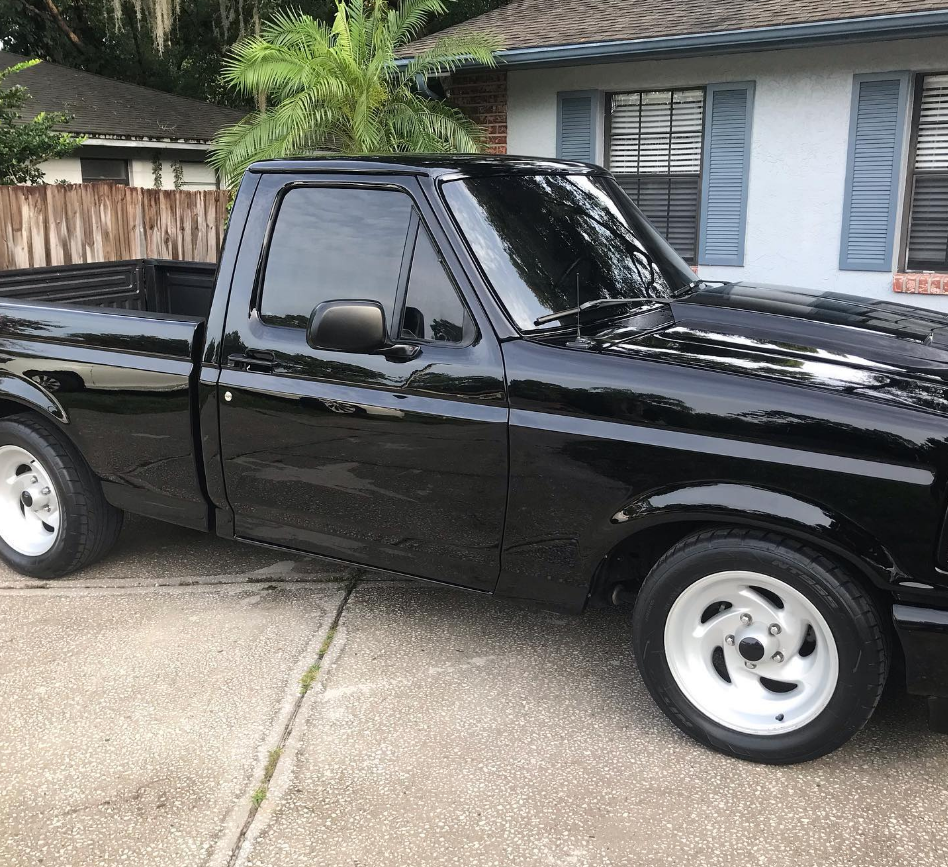 Black Ford pickup truck parked in front of a house, featuring white wheels.