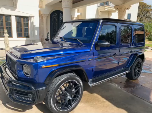 Blue Mercedes-Benz G-Wagon parked in front of a house with black rims.