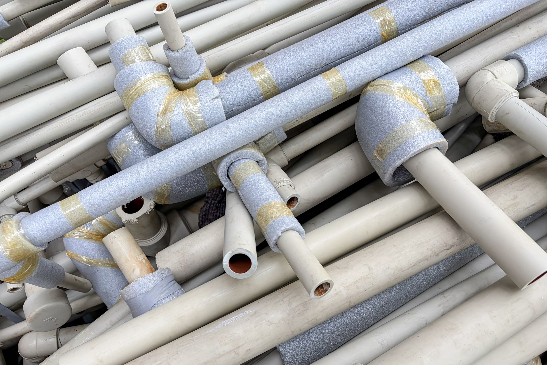 White PVC pipes and elbow fittings wrapped in blue foam insulation, ready for plumbing stack work.