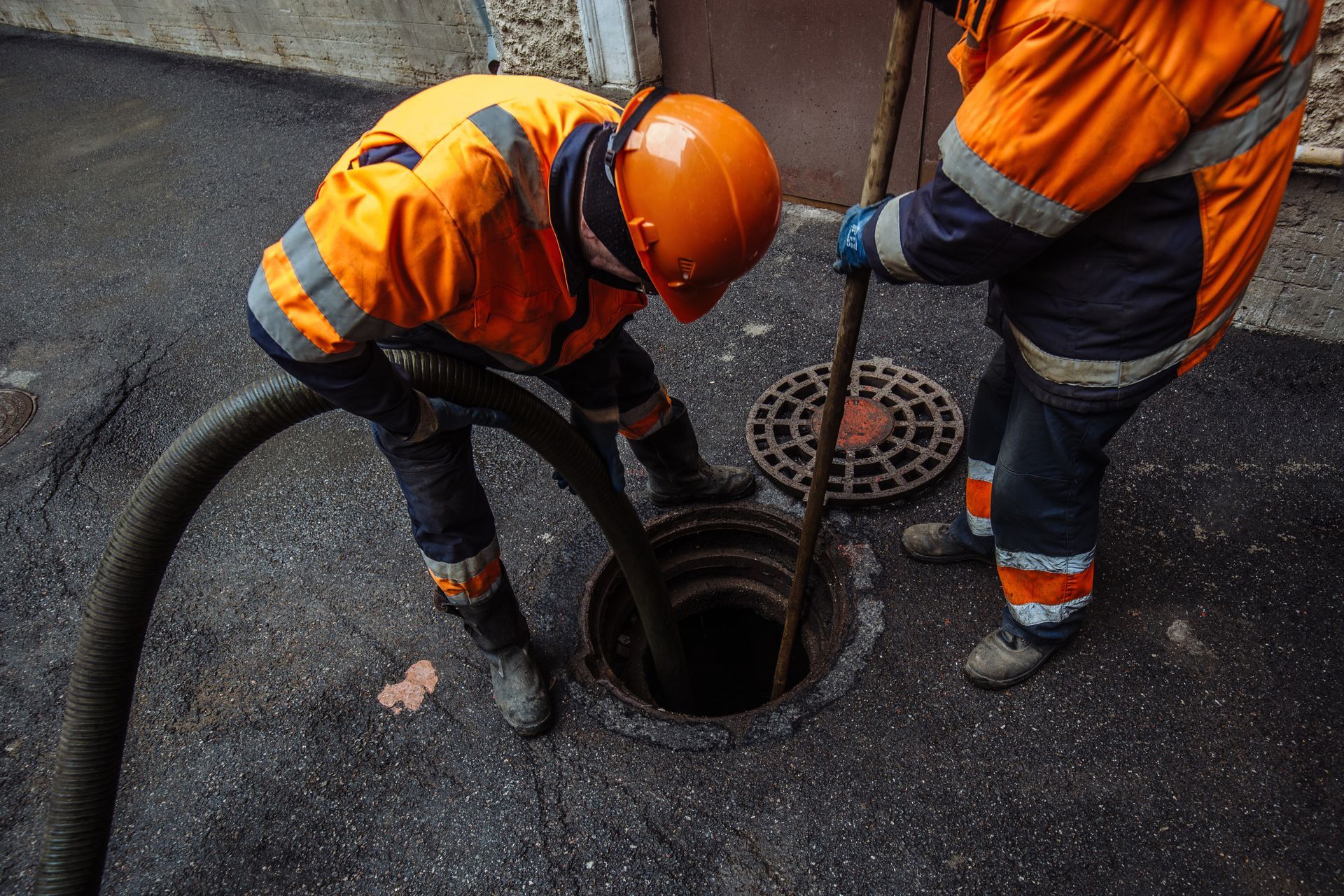 Workers performing sewer or drain cleaning through an open manhole using vacuum equipment