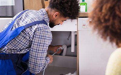 Plumber clearing a clogged drain under a sink Plumber clearing a clogged drain under a sink
