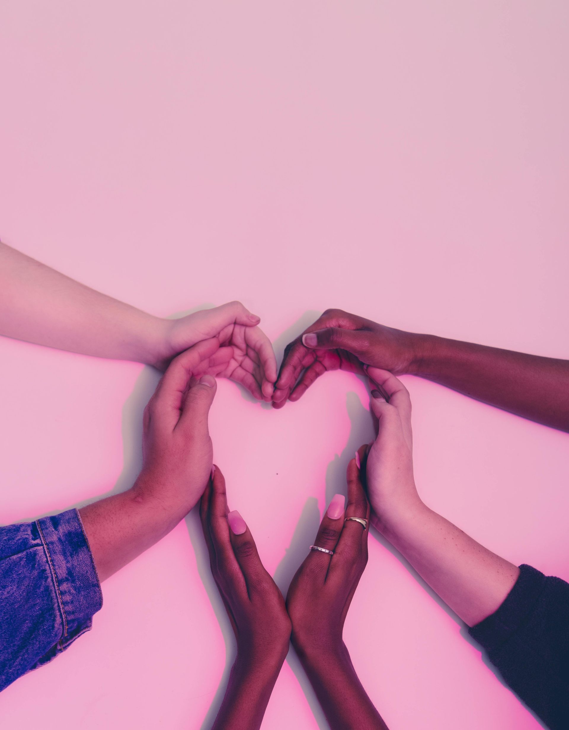 Hands from diverse people forming a heart.