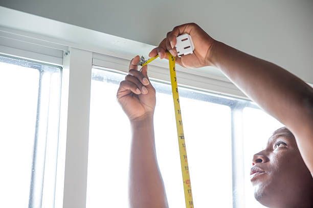 Hands using tape measure to accurately measure window frame for home improvement installation.