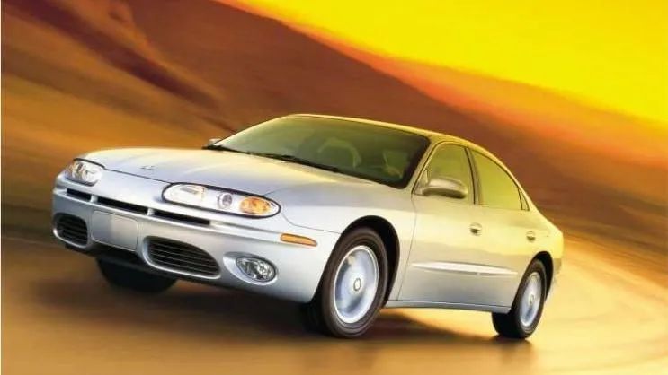 Silver sedan driving on a golden road against an orange sky