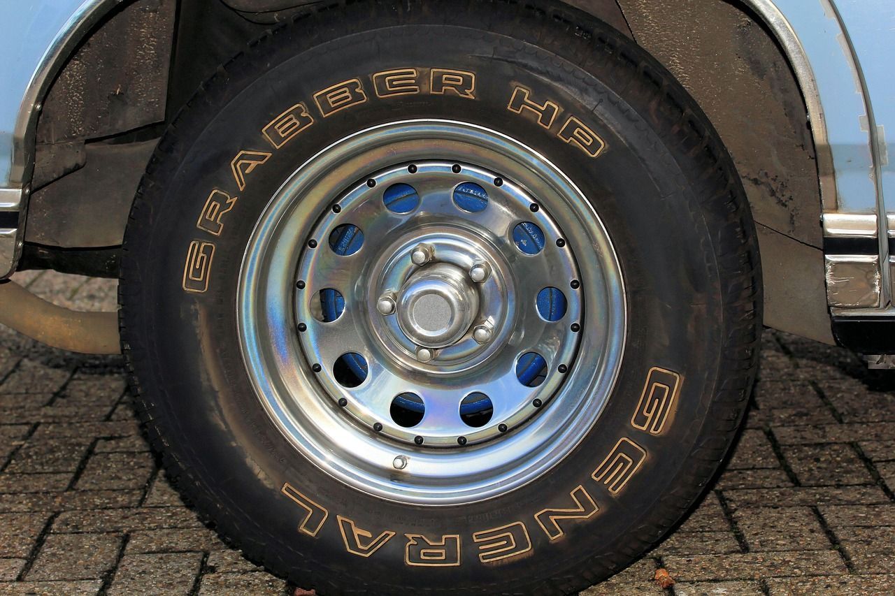 Close-up of a car wheel with a shiny silver rim and black General tire on a cobblestone surface