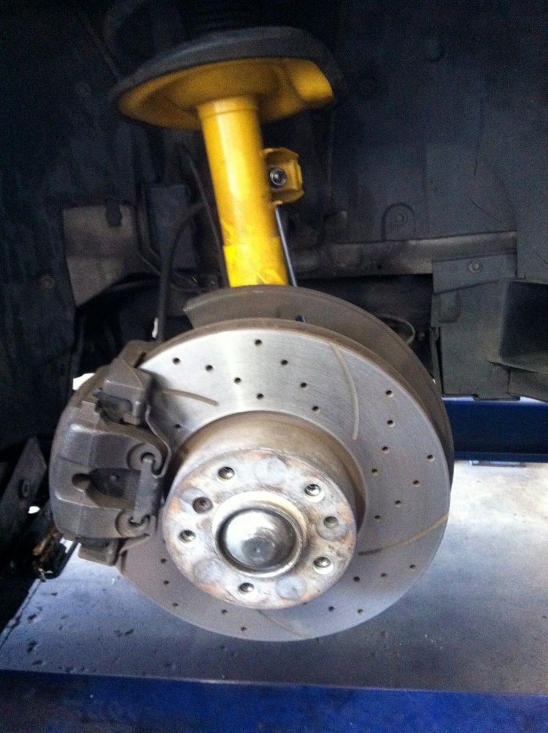 Car wheel brake rotor and caliper with yellow suspension in a workshop, close-up view