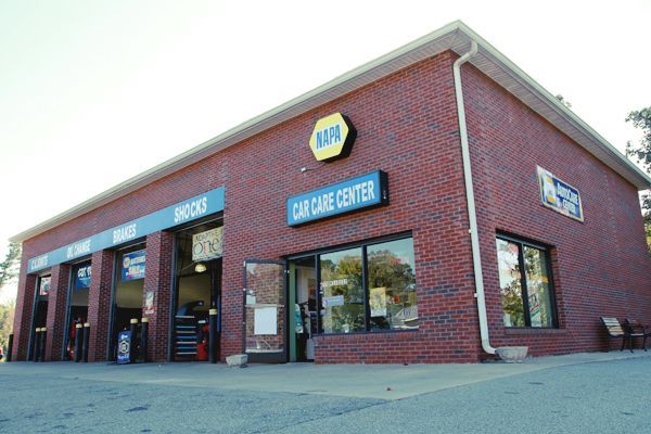 A brick auto care center with blue signs and open service bays on a street corner.