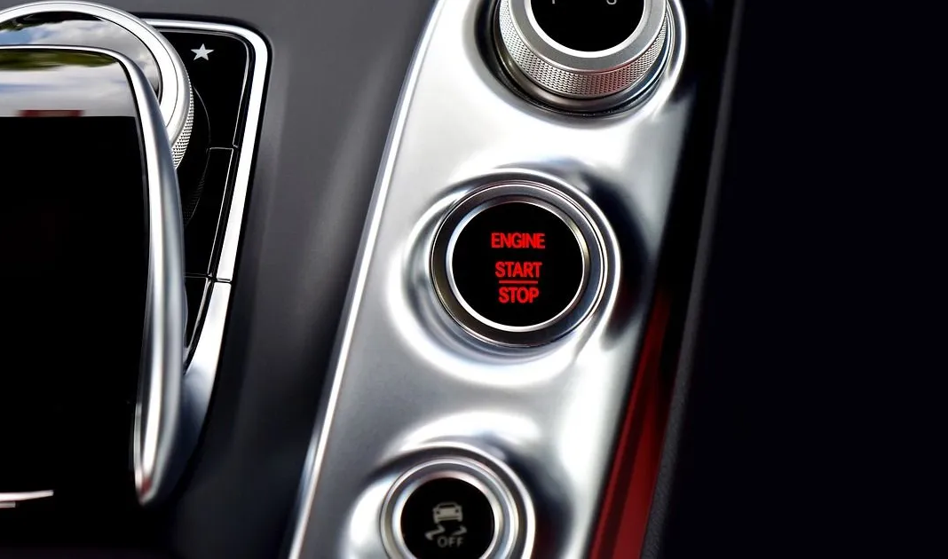 Close-up of a car dashboard with a red start-stop button and silver control panel