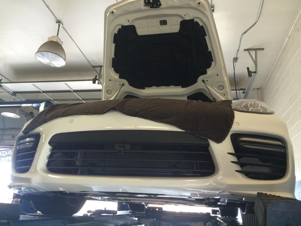 White car with hood open in a garage, front grille and headlights visible