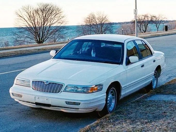 White sedan parked by a waterfront road at sunset