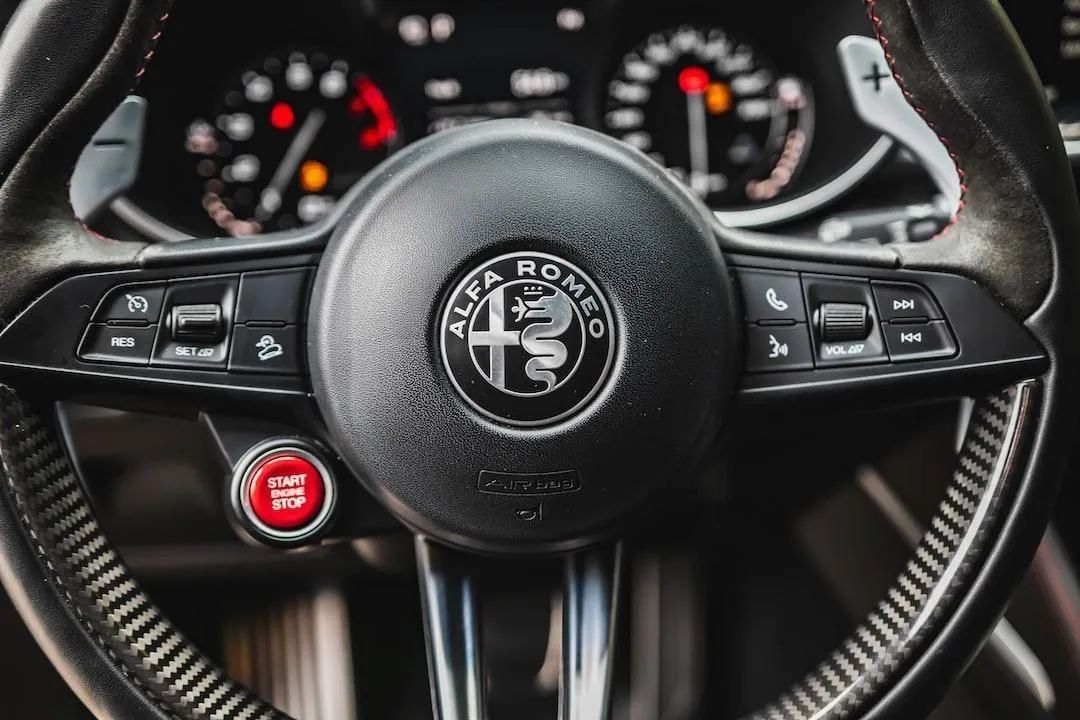Alfa Romeo steering wheel and dashboard with illuminated gauges and red start button