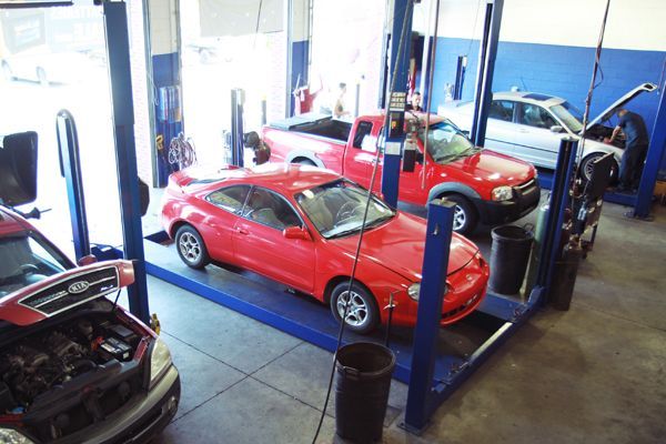 Red sports car in an auto shop, with a red pickup on lifts in the background.